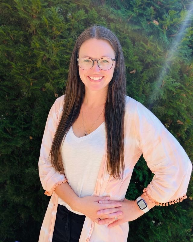 Justine Craigen, Registered Massage Therapist, smiling outdoors in front of a green hedge.